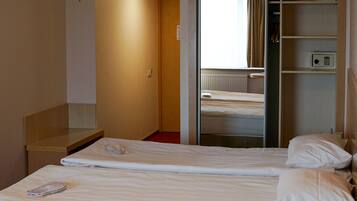 Hotellihuone, jossa on kaksi sänkyä, punainen matto, puinen penkki, vaatekaappi ja pieni pöytä.