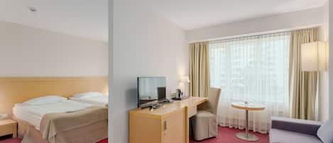 Una habitación de hotel con cama, escritorio, silla, sofá y ventana con cortinas.
