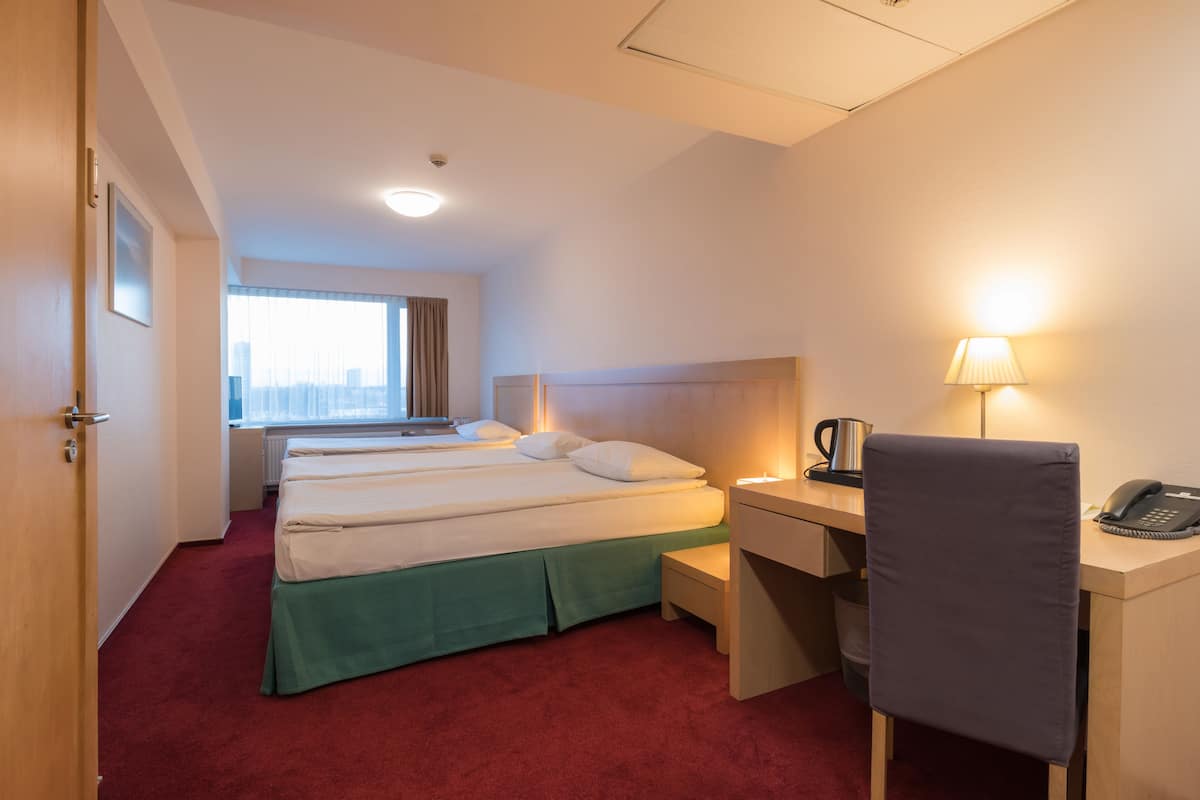 A hotel room with a bed, a desk with a lamp, a chair, and a window with a view.