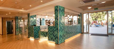 Un área de recepción con un revestimiento de pared de diseño tablero de ajedrez, un mostrador de recepción y una puerta de vidrio que da al exterior.