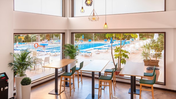 A modern indoor dining area with large windows overlooking a pool and outdoor seating. - Hotel Gala Placidia (Benidorm)