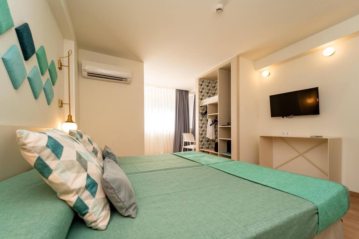 A room with a bed, a TV mounted on the wall, and a wardrobe with a mirror.