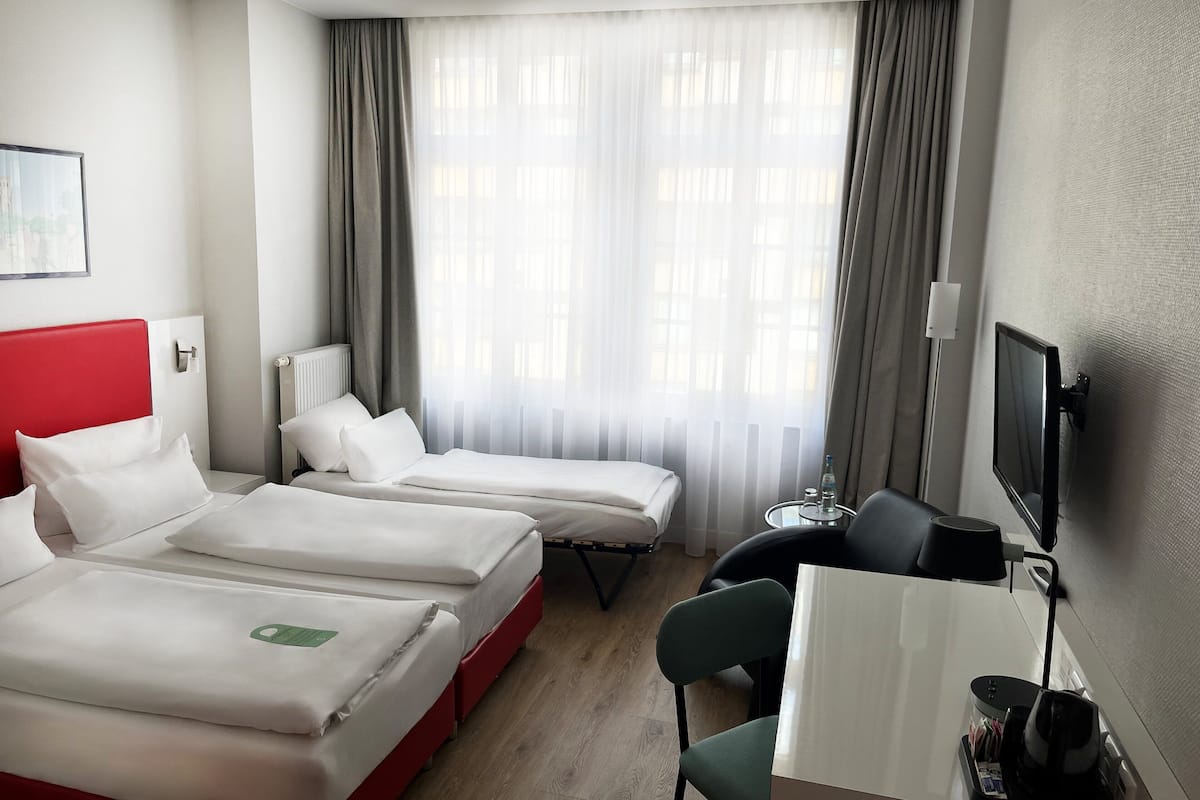 A hotel room with two beds, a desk, a chair, a TV, and a window with curtains.