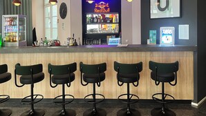 A bar area with a neon Red Bull sign, a clock, and a counter with various bottles and glasses. - Garner Hotel Berlin - Checkpoint Charlie by IHG (Berlin)