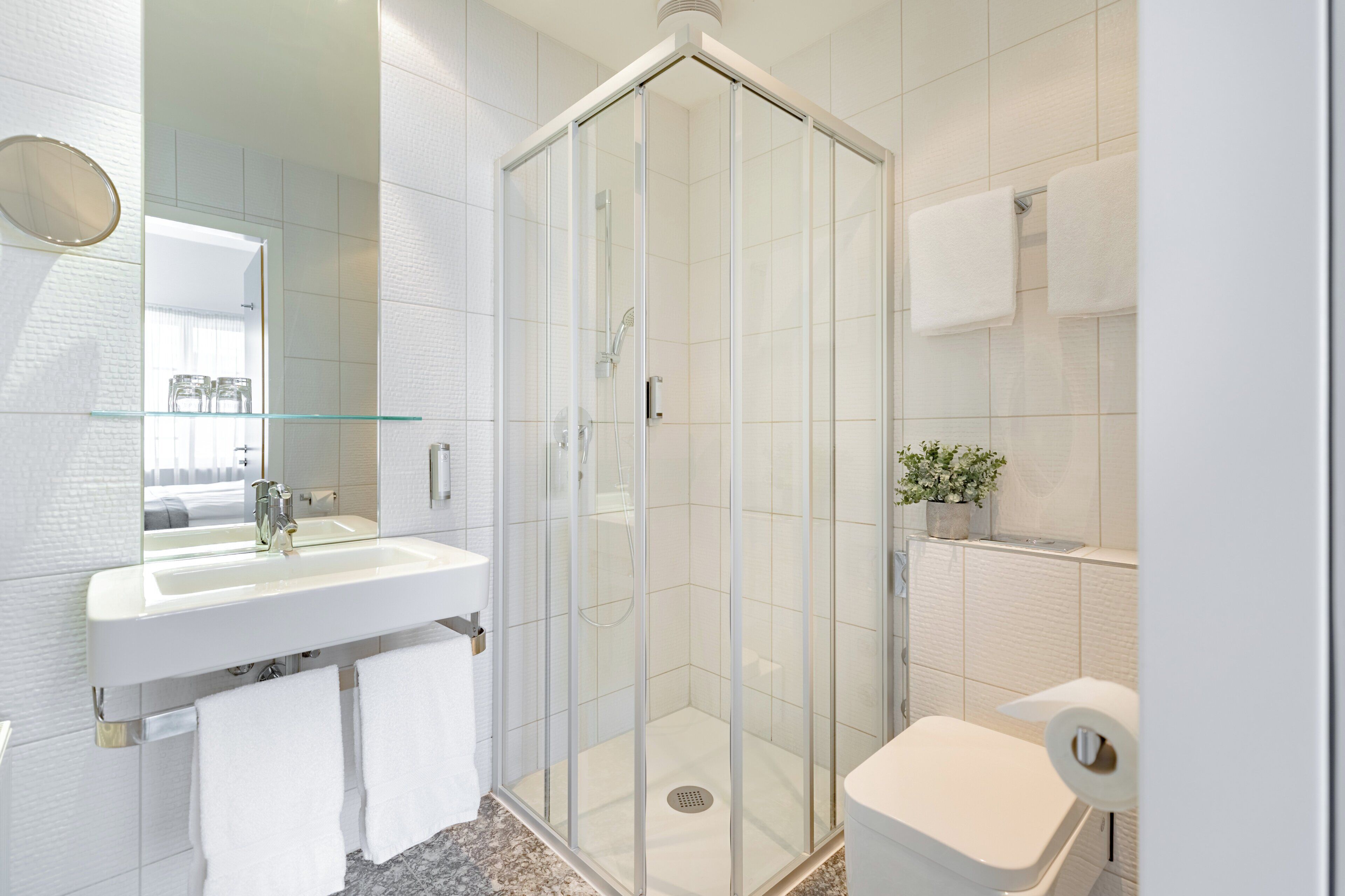 Un baño moderno con ducha de vidrio, lavamanos blanco y un inodoro.