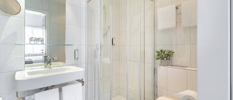 Un baño moderno con ducha de vidrio, lavamanos blanco y un inodoro.