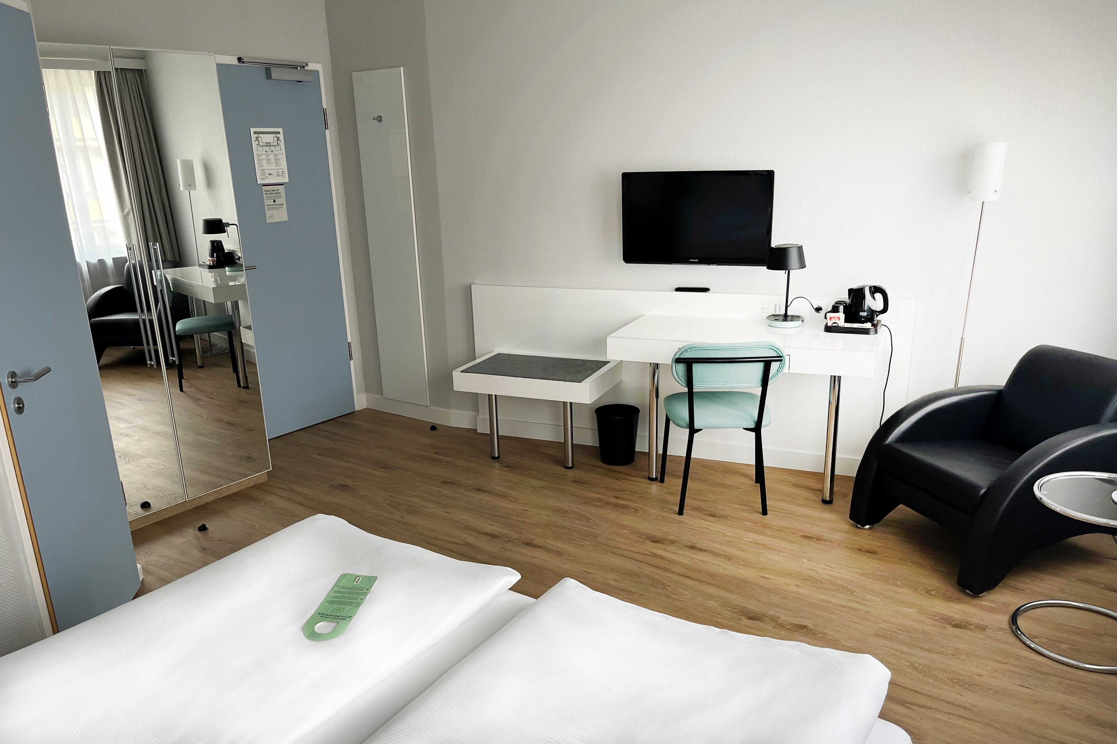 A hotel room with a bed, a desk with a chair, a TV, and a lamp.