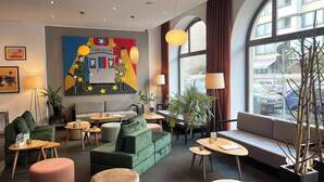 A modern hotel lobby with a green sofa, round ottomans, and a large painting on the wall. - Garner Hotel Berlin - Checkpoint Charlie by IHG (Berlin)