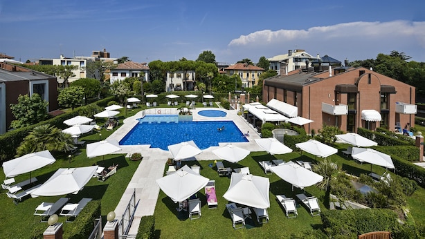 Zona de piscina en la azotea con varias sombrillas y sillas de descanso, rodeada de edificios y follaje.