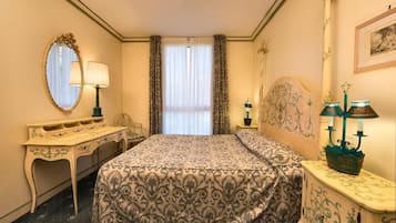 A hotel room with a bed, a desk, a chair, a lamp, and a mirror.