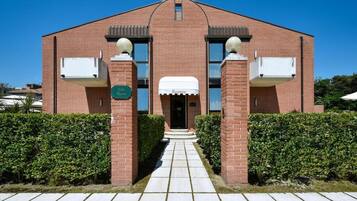 Een gebouw van baksteen met een centrale ingang, twee zij-ingangen met luifels, en een heldere lucht.
