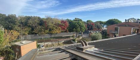 A rooftop with a metal roof, a brick wall, and a view of trees and a fence.