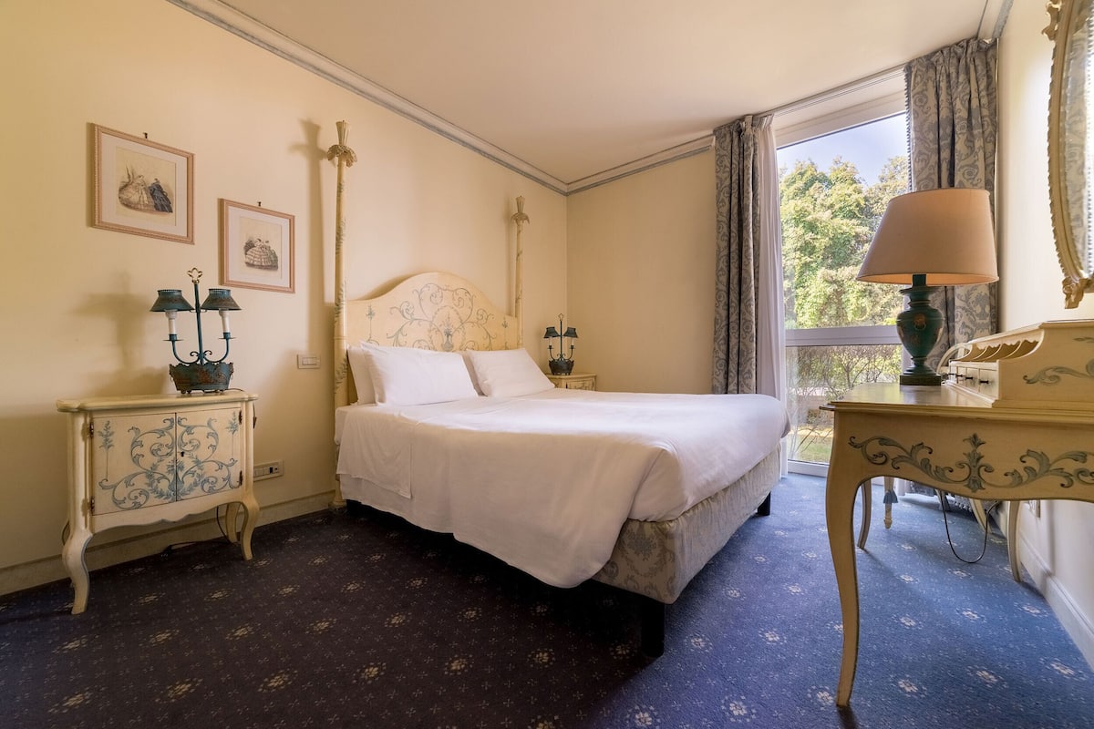 A bedroom with a large bed, a nightstand, a dresser, and a window with curtains.