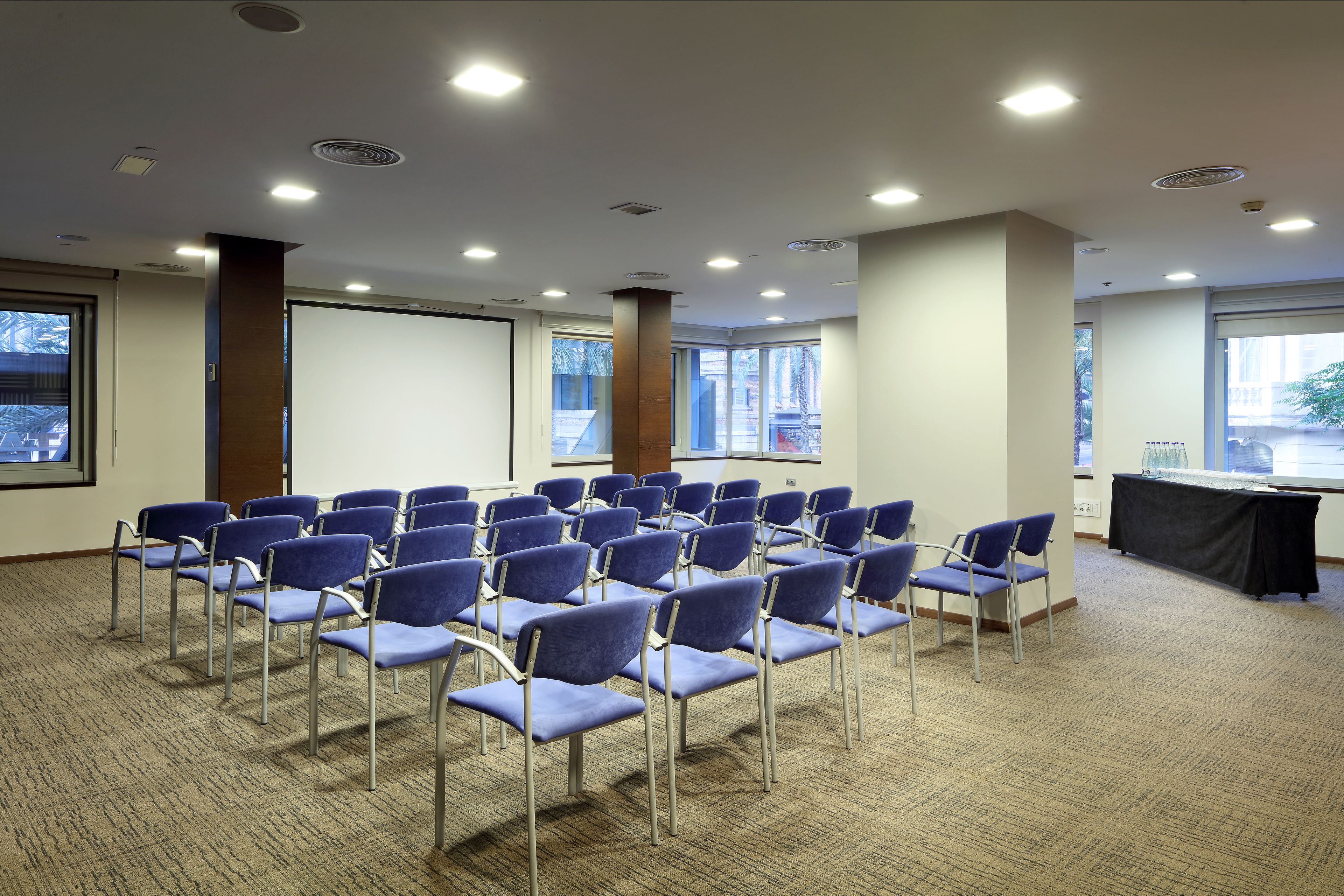 A conference room with rows of blue chairs, large windows, and a black table.