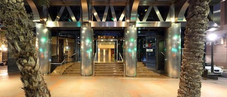 La entrada al hotel Eurostars Lucentum, con un diseño moderno, presenta un acceso destacado, una escalera y palmeras.