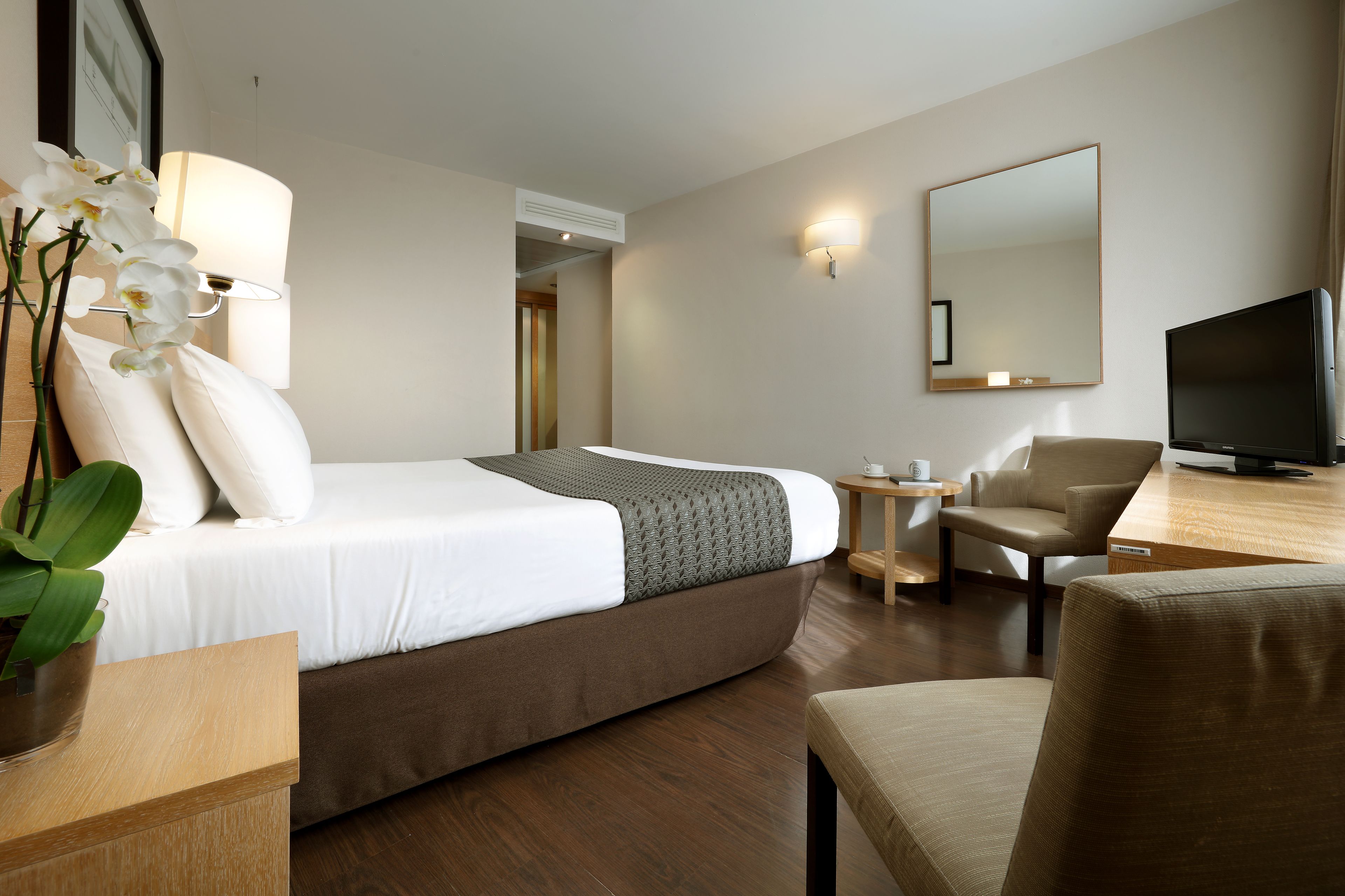 Ein Hotelzimmer mit Bett, Schreibtisch, Stuhl, Fernseher und Spiegel.