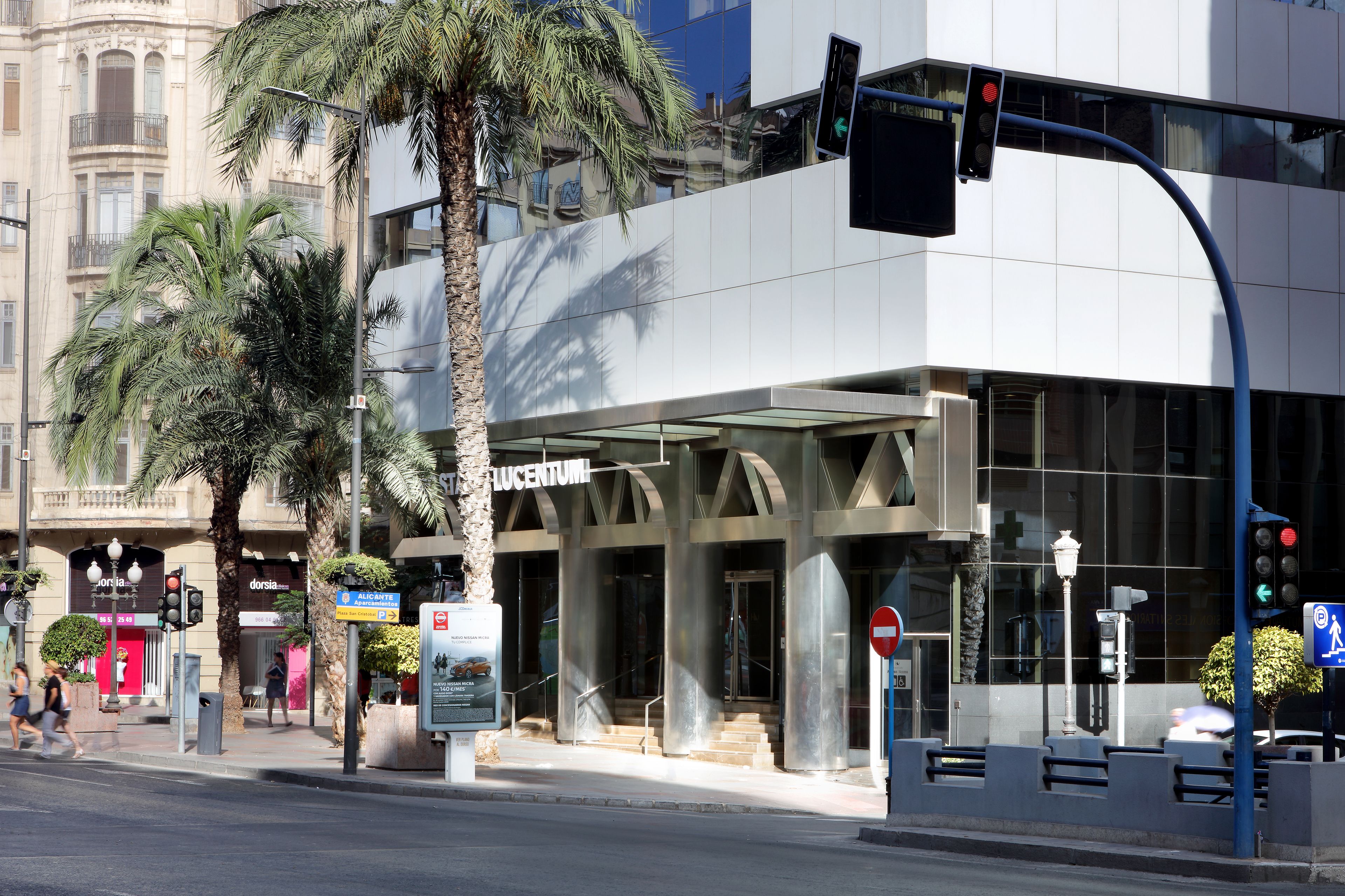 A modern building with a glass facade, palm trees, and a pedestrian crossing.
