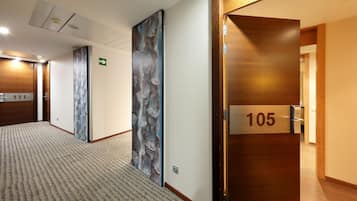 Un pasillo de hotel con pisos alfombrados, puertas de madera y un cuadro abstracto grande en la pared.