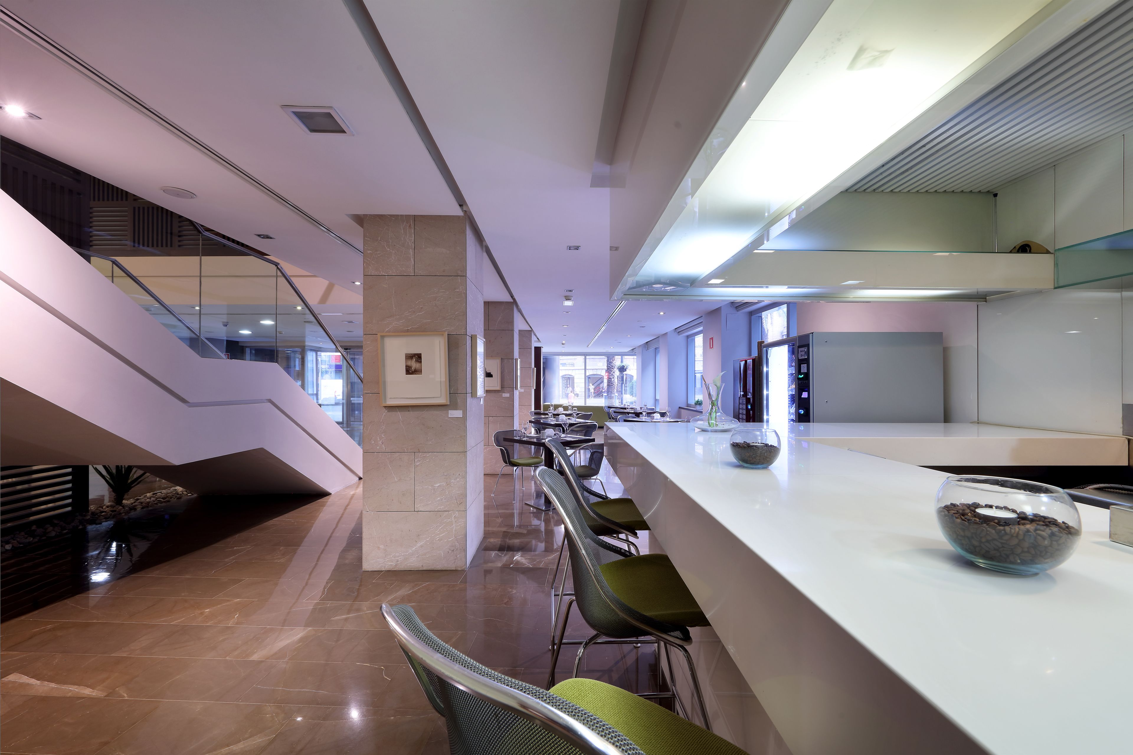Un moderno vestíbulo de hotel con una escalera central, un área de estar y una recepción.