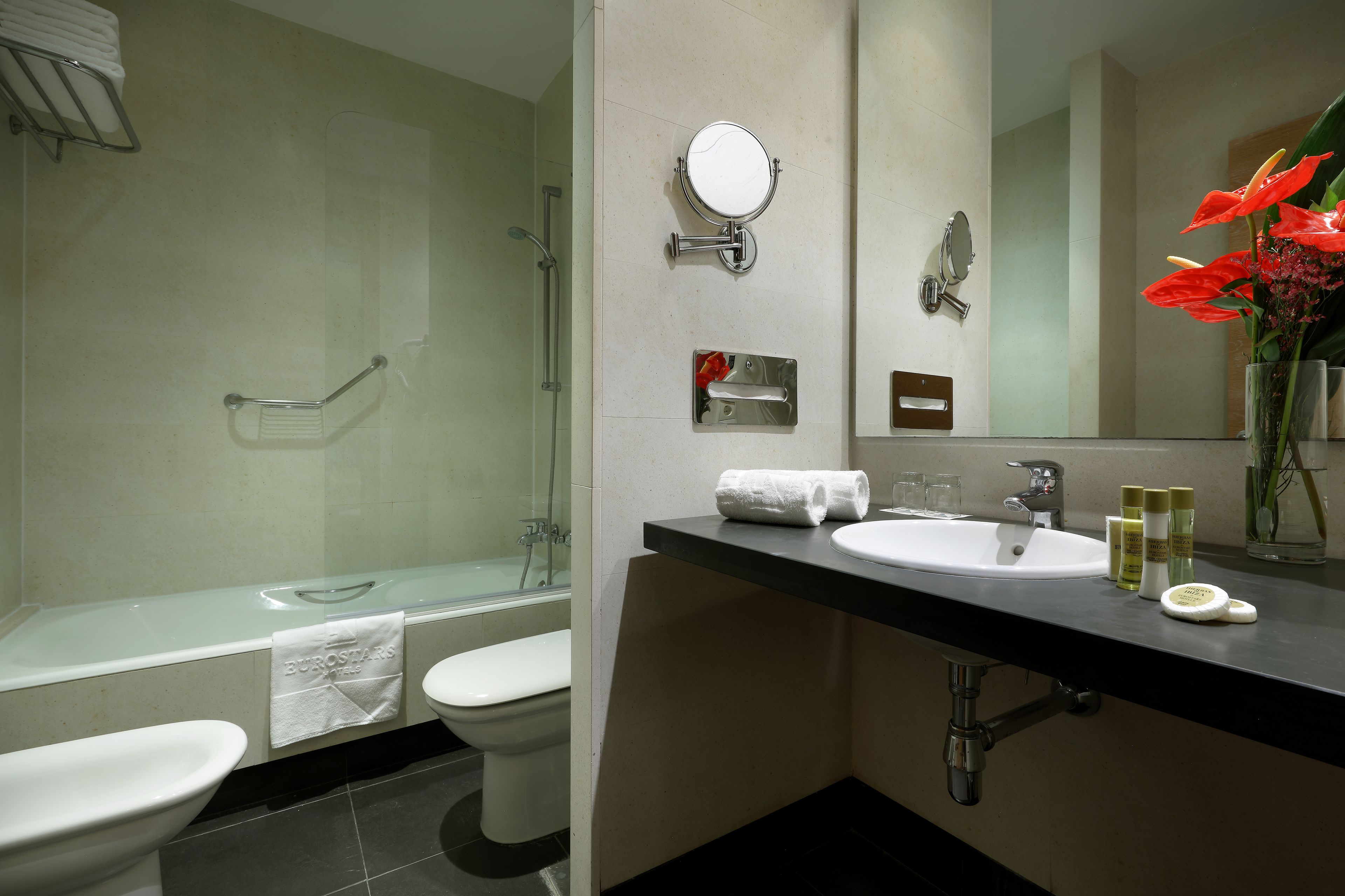 A modern bathroom with a glass-enclosed shower, a sink with toiletries, and a mirror.