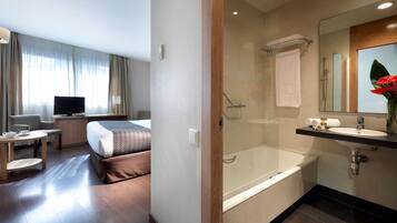 Une chambre d’hôtel moderne équipée d’un lit, d’une table de chevet, d’une télévision et d’une salle de bain avec baignoire et douche.