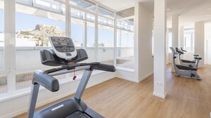 Un gimnasio con cinta de correr y elíptica, en una sala luminosa con ventanales grandes.