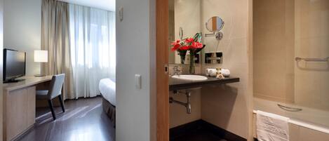 Un baño de hotel con lavamanos, espejo y ducha.