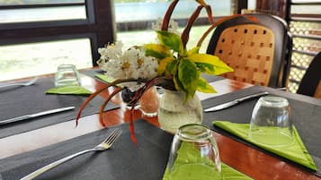 A dining table set with a vase of flowers, a glass jar, and cutlery.