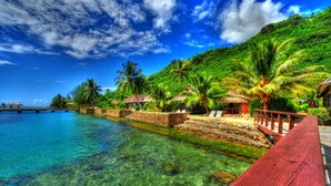 A tropical beach resort with clear waters, palm trees, and a wooden walkway. - Hotel Kaveka (Moorea-Maiao)