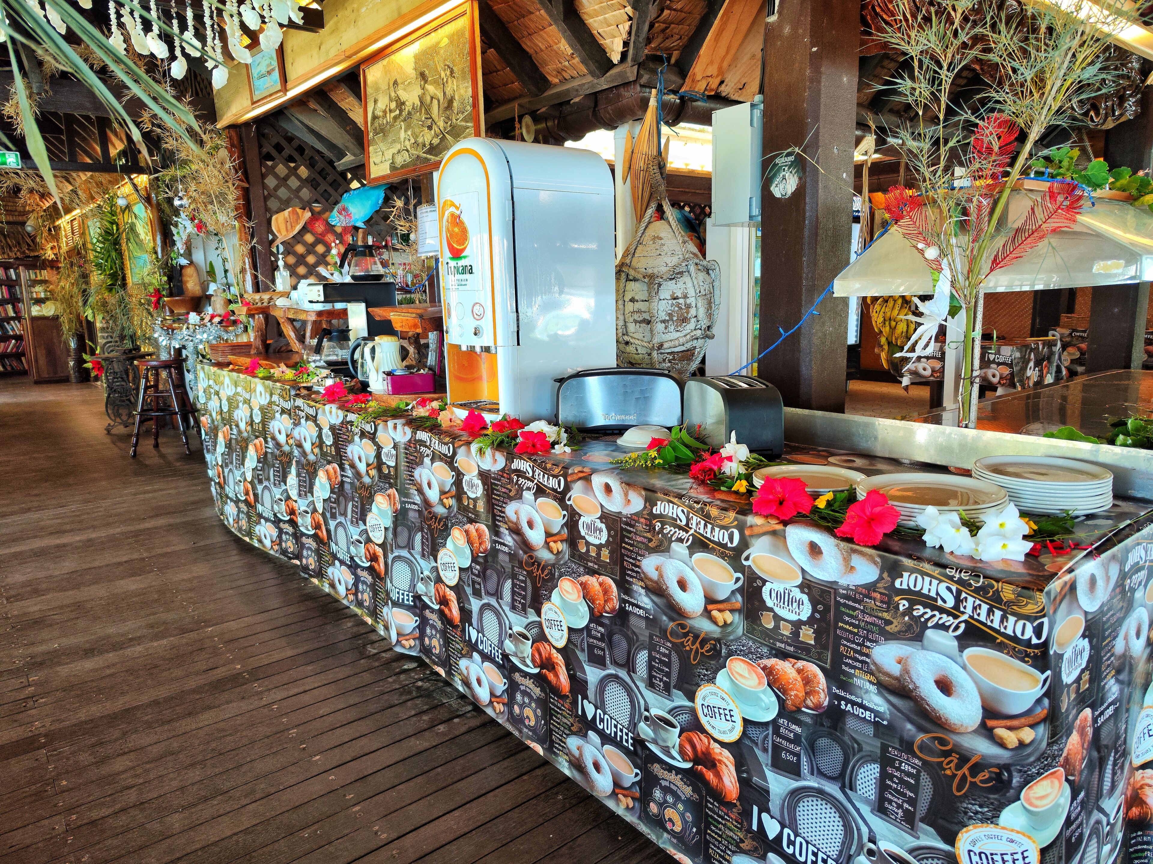 Una cafetería con una barra larga adornada con motivos de café, una máquina de café y una decoración interior de madera rústica.