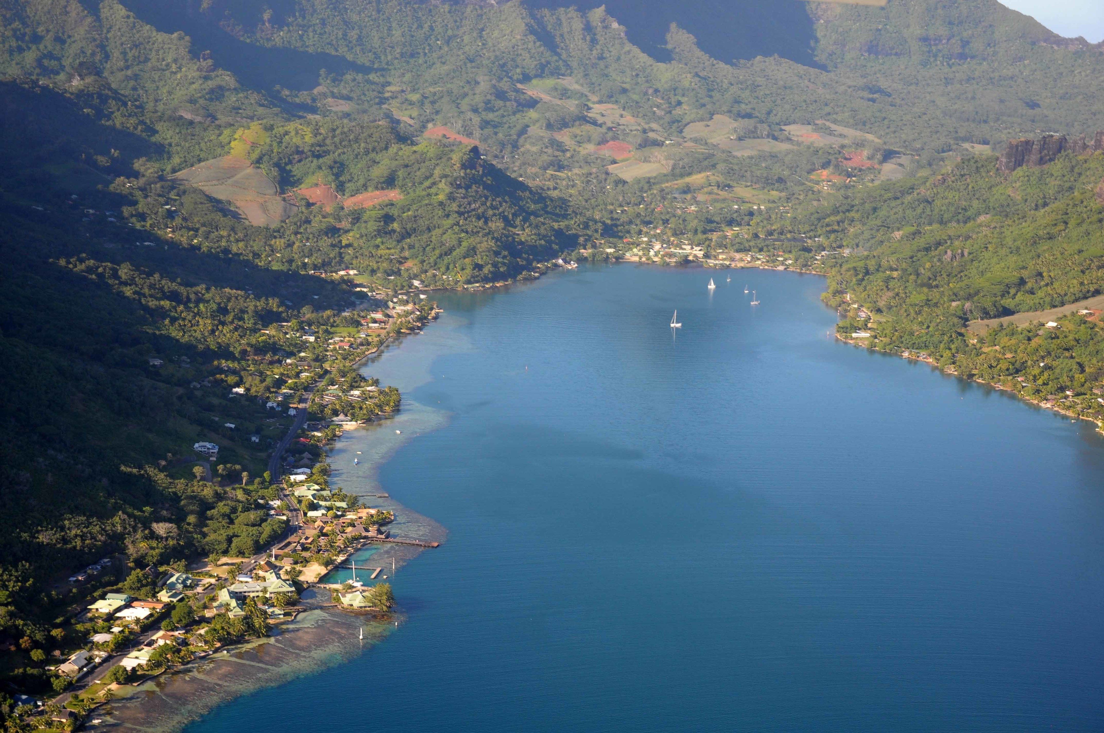 An aerial view of a coastal town with a large bay, surrounded by hills and greenery.