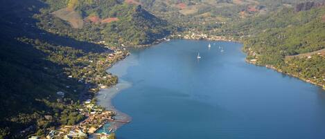 An aerial view of a coastal town with a large bay, surrounded by hills and greenery.