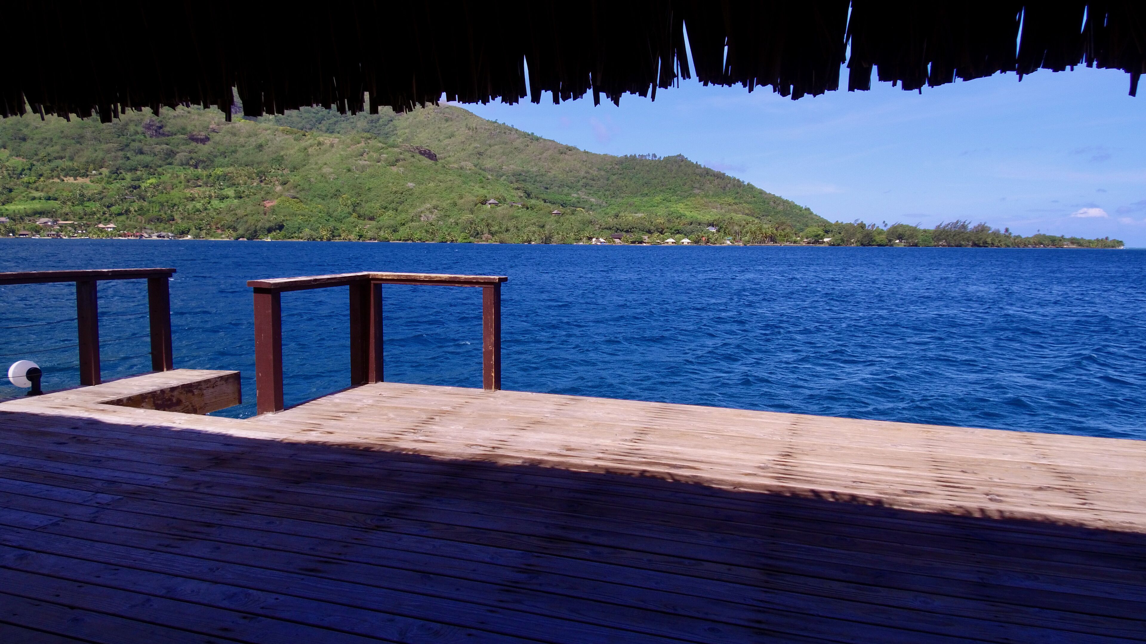 A wooden pier extending into a body of water with a green hillside in the background.