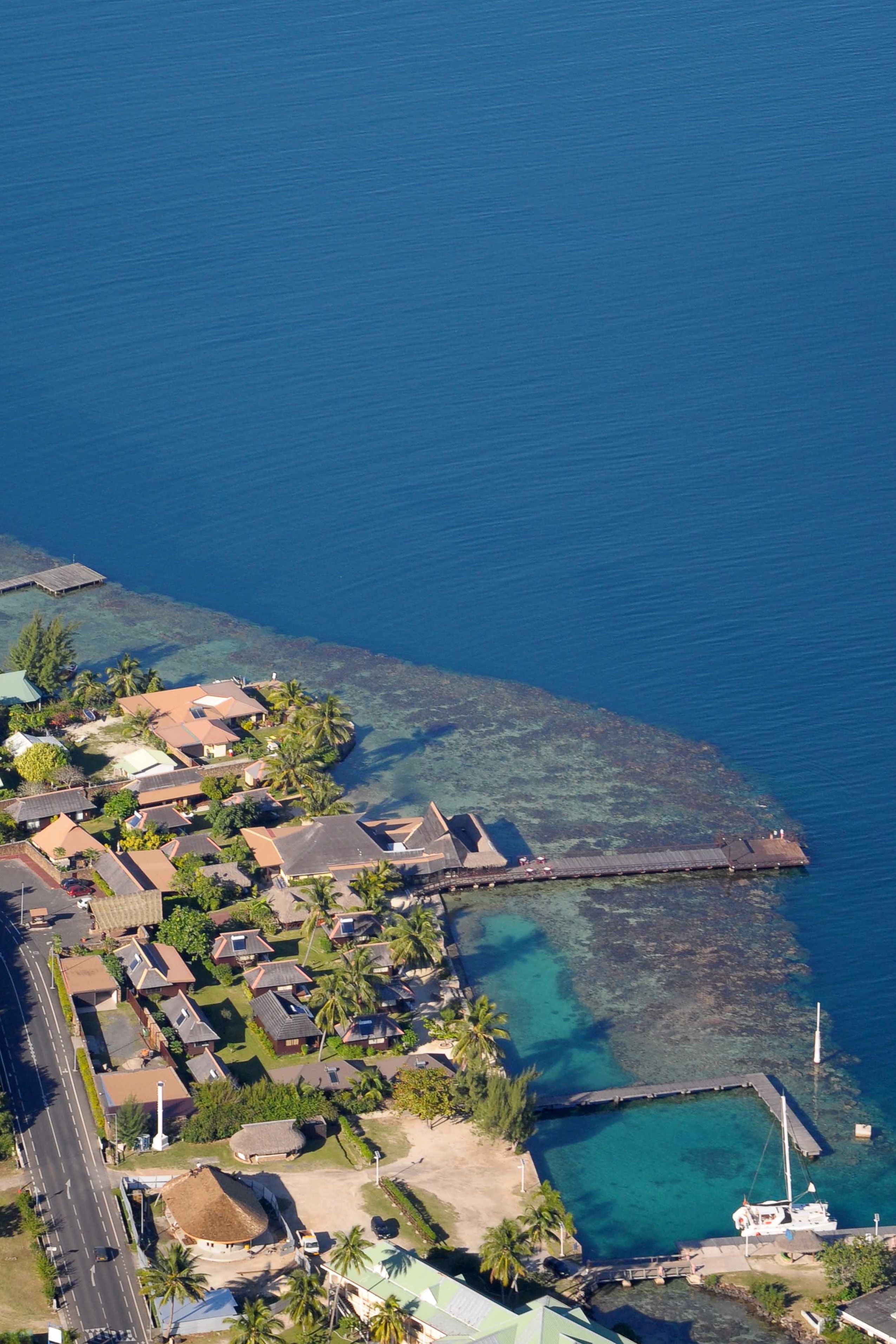 Vista aérea de una zona residencial costera con casas, un muelle y agua azul cristalina.
