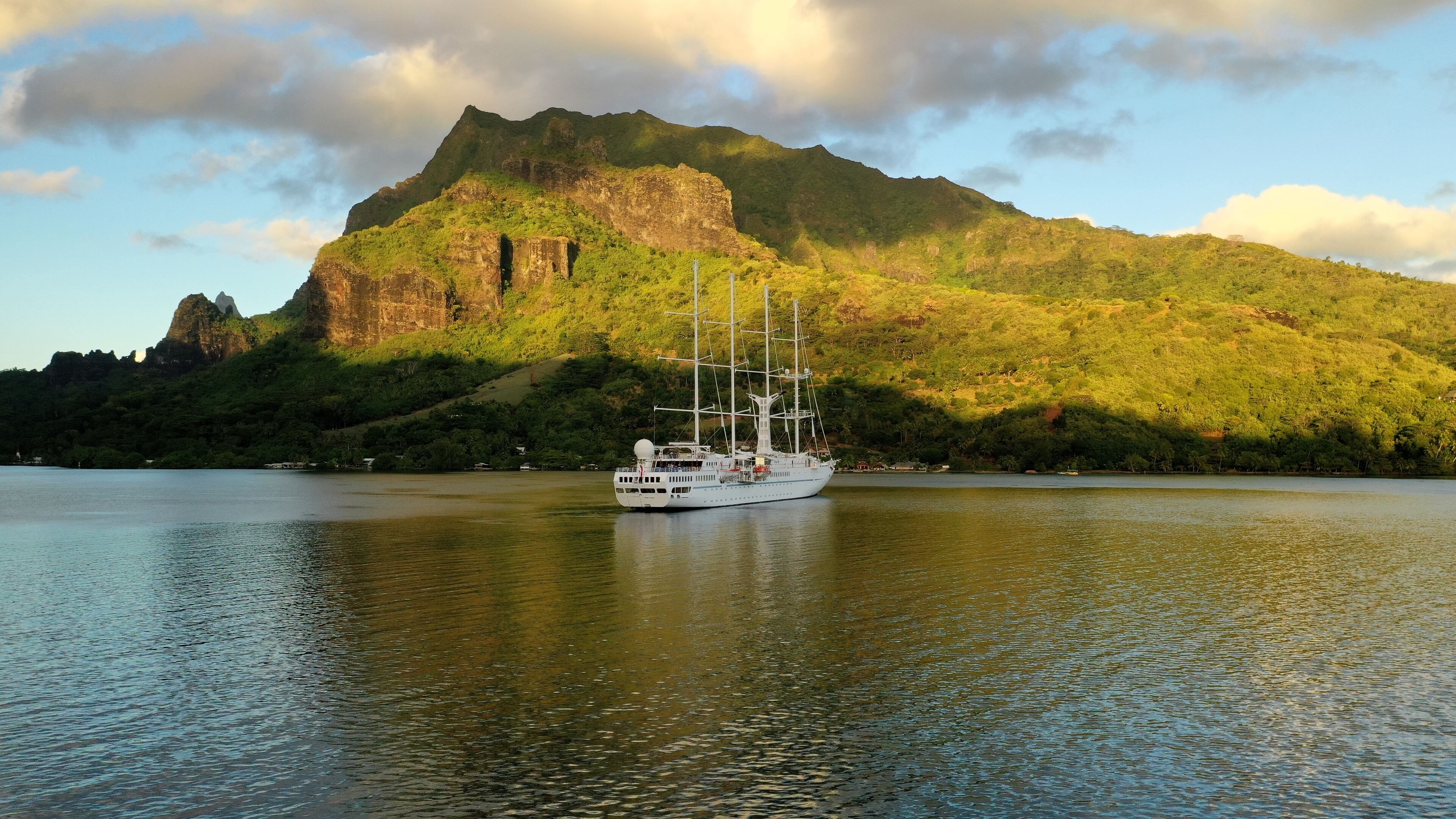 A large white yacht on calm water with a mountain in the background.
