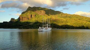 A large white yacht on calm water with a mountain in the background.
