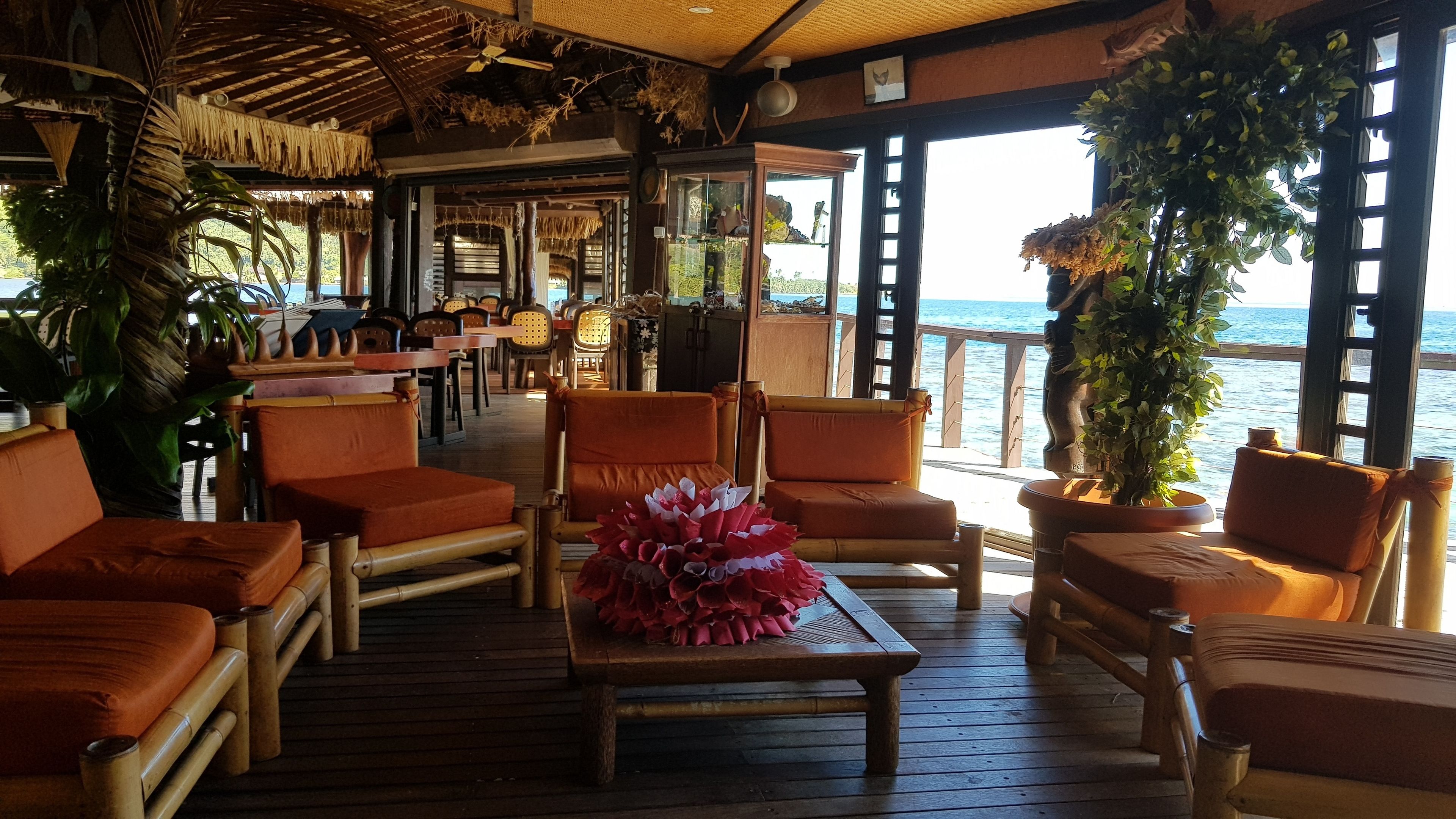 A deck with wooden furniture, potted plants, and a view of the sea.