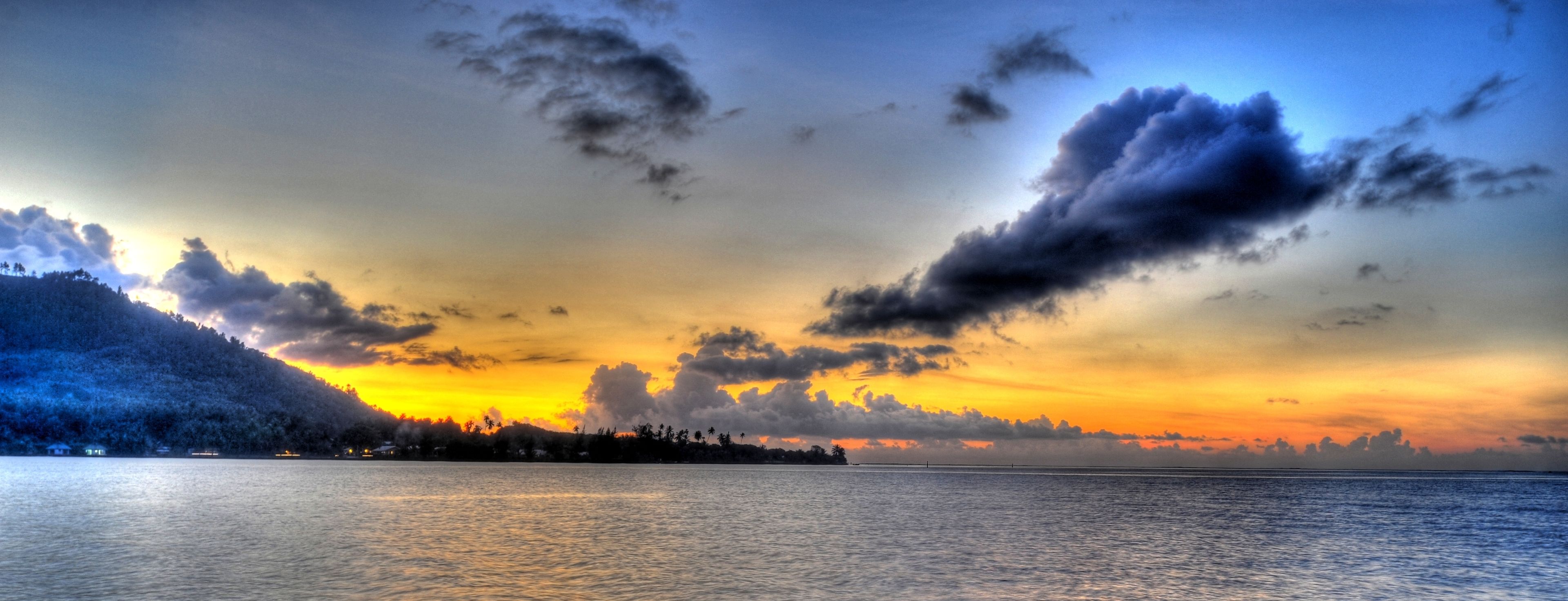 A sunset over a calm body of water with a distant shoreline.