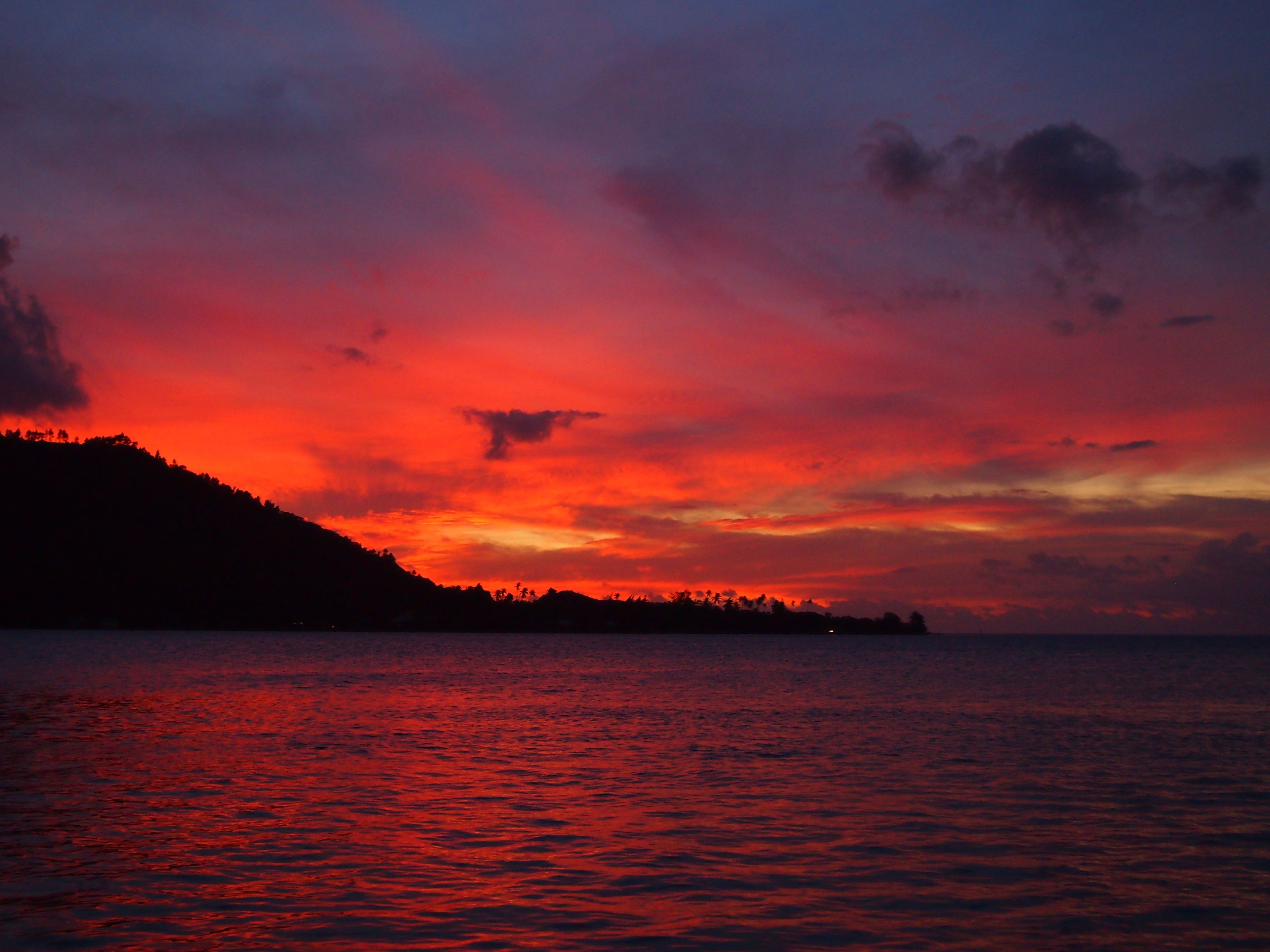 A sunset over a body of water with a silhouette of a hill in the foreground.