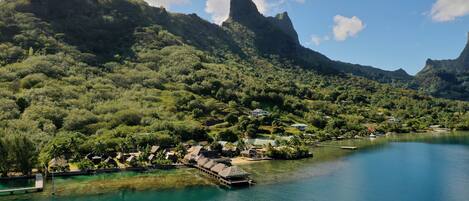 Un resort costero con bungalows sobre el agua, exuberante vegetación y un lago azul cristalino.