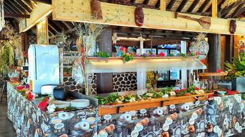 Una cafetería rústica con techo de paja, vigas de madera y una barra decorada con objetos y plantas de café.