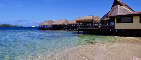 Overwater bungalows met rieten daken, helder turquoise water en een boot in de verte.