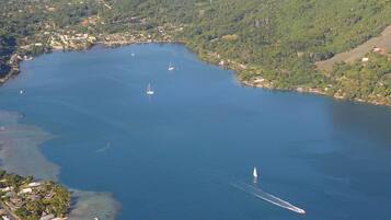 An aerial view of a coastal town with a large body of water, several boats, and surrounding green hills.