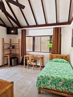 Una habitación con cama, escritorio, silla, televisor y ventana con cortinas.