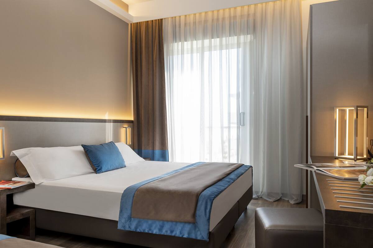 A modern hotel room with a large bed, bedside lamps, a desk, and a TV.
