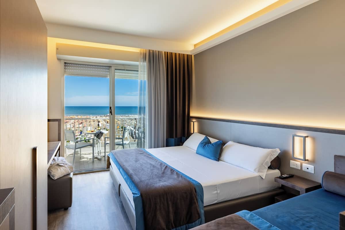 A hotel room with a balcony, a bed, a desk, and a chair.