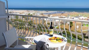 A balcony with a table set for a meal, a bottle of wine, and a view of the beach and ocean. - Hotel Continental Rimini (Rimini)