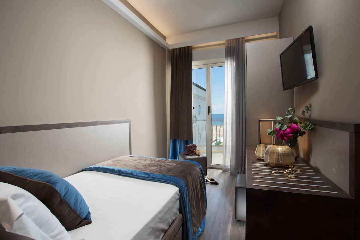 A hotel room with a bed, a small table with a vase of flowers, and a television mounted on the wall.