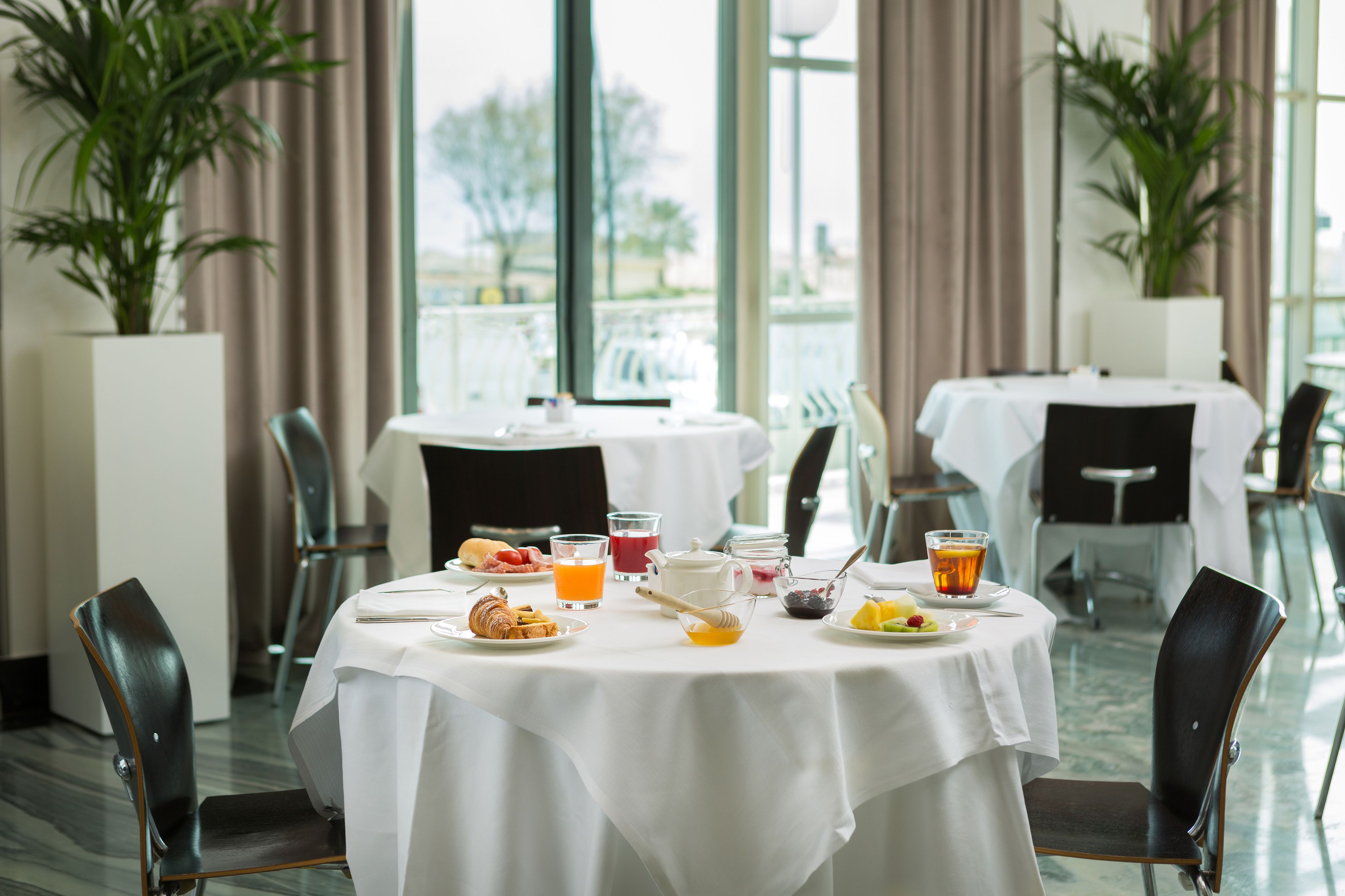 Un espace repas avec des tables rondes, des chaises et une variété d’aliments pour le petit-déjeuner.