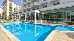 A swimming pool with lounge chairs and umbrellas, surrounded by a building with large windows and balconies. - Hotel Continental Rimini (Rimini)